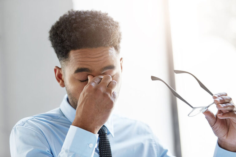 Frustrated young Afro American businessman feeling stressed after hard work, having tired expression, keeping his hand on eyes, resting for minute. Overworked mixed race male feeling stressed