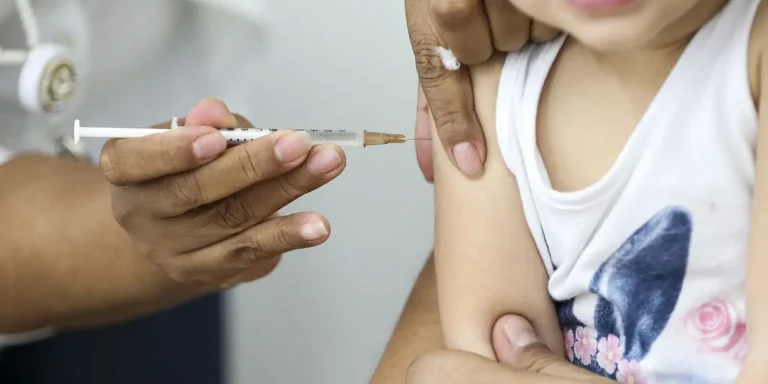 Profissional de saúde aplica vacina em criança em posto de saúde
